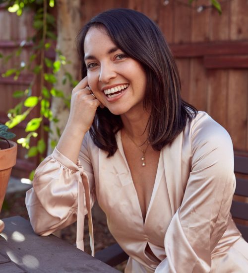 A vertical shot of a pretty female with a pink silk dress sitting in an outdoor cafe